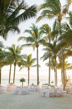 an empty beach with palm trees and white linen tables set up for a wedding reception