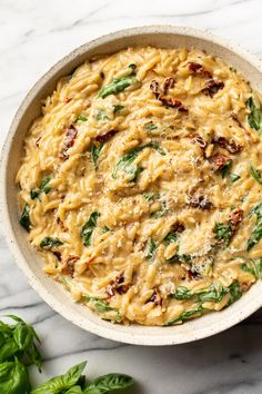 a white bowl filled with pasta and spinach on top of a marble countertop