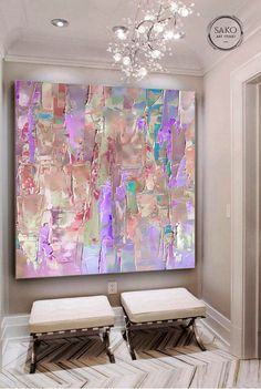 an abstract painting hangs on the wall above two stools in front of a chandelier