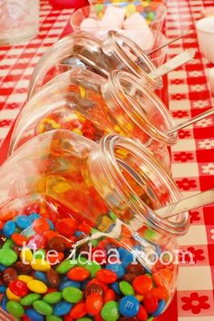 there are many jelly beans in the glass containers on the red and white checkered tablecloth