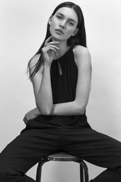 a woman sitting on top of a stool with her hand under her chin and looking at the camera