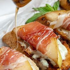 two pieces of bread with meat and cheese on them, being drizzled with honey