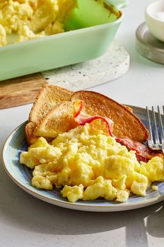 a plate with toast, eggs and bacon on it next to a bowl of scrambled eggs