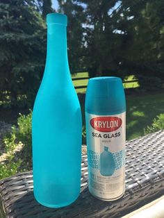 a blue glass bottle next to an empty plastic bottle on a picnic table in the sun