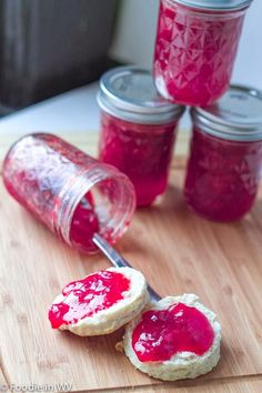 jam being spread on top of two biscuits with a jar in the back ground next to it