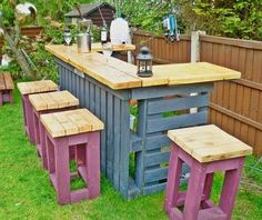 an outdoor bar made out of pallet wood with stools on the grass in front of it