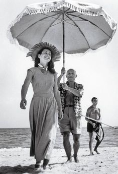 a black and white photo of two people under an umbrella on the beach with other people in the background