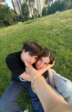 two people sitting in the grass with their arms around each other and one person's hand on his shoulder