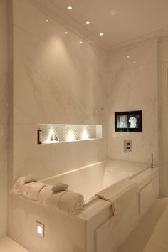 a white bath tub sitting next to a toilet under a tv mounted on the wall