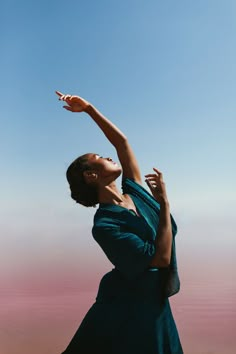 a woman in a blue dress reaching up to catch a frisbee with her hand