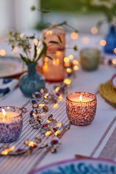 a table topped with candles and plates covered in glass vases next to each other