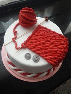 a red and white cake decorated with yarn and buttons on a black tableclothed surface