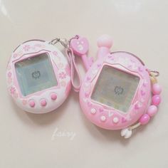 two pink electronic devices sitting next to each other on a white surface with hearts and flowers