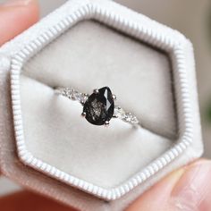 a close up of a person holding an engagement ring in a small white gift box