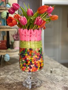 a glass vase filled with candy and flowers on top of a marble counter topped with candies