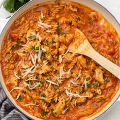 a large pot filled with pasta and meat on top of a table next to a wooden spoon