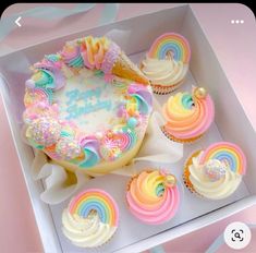 a box filled with cupcakes covered in frosting and rainbow icing on top