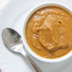 a white plate topped with a bowl of soup and a spoon on top of it