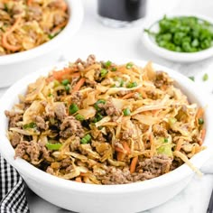 two white bowls filled with noodles and meat on top of a marble table next to green beans