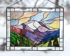 a stained glass window hanging from a chain in front of snow covered trees and mountains