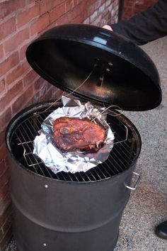 a bbq with some meat on top of it next to a brick wall and a person