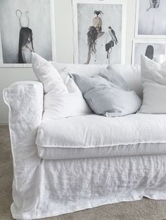 a white couch with pillows on it in front of pictures and photos hanging on the wall