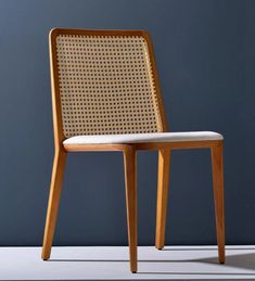 a wooden chair with a white cushion on the seat and backrest, against a blue wall