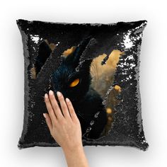 a person's hand on a black sequin pillow with an image of a cat