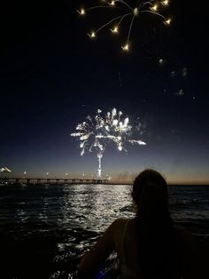 fireworks are lit up in the night sky over water with people sitting on rafts watching