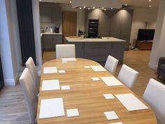 a large wooden table with white chairs in a living room next to an open kitchen