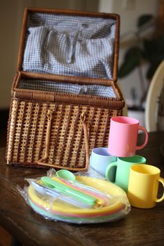 a wicker basket with cups, plates and spoons next to it on a table