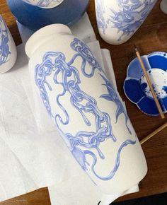 some blue and white vases sitting on top of a wooden table next to paintbrushes