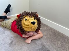 a little boy laying on the floor wearing a crocheted lion hat