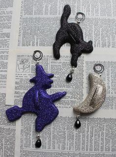 three different colored cat charms sitting on top of an open newspaper with black and silver glitter