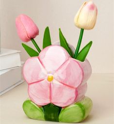 three pink flowers in a green vase on a white table next to a stack of books