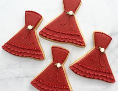 decorated cookies in the shape of dresses on a white tablecloth with red icing