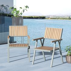 two wooden chairs sitting next to each other on a patio near the water's edge