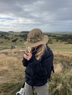 a woman in a hat is looking at her cell phone while standing on a hill