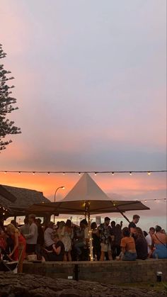 a group of people standing on top of a beach next to the ocean at sunset