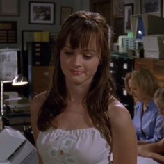 a woman in a white dress sitting at a desk with two other people behind her