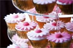 cupcakes with pink frosting and white flowers on them are stacked on a cake stand