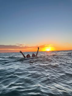 a woman floating in the ocean at sunset with her arms up and hands out to the sky