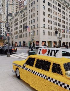 a taxi made out of flowers in the middle of a city street with buildings and cars