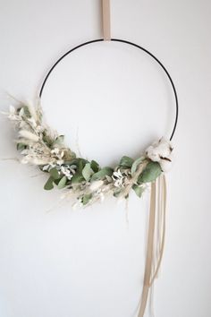 a circular wreath with white flowers and greenery hanging on the wall in front of a white wall