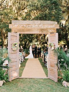 the wedding ceremony took place in front of an open wooden door, with flowers and greenery on either side