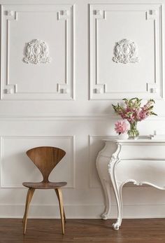 a white table and chair in front of a wall with decorative paneling on it