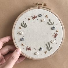 a hand is holding a small embroidery hoop with shells and starfishs on it