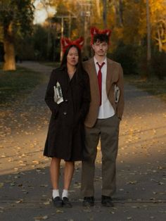 a man and woman are dressed up in devil ears, standing on a road with leaves all around them