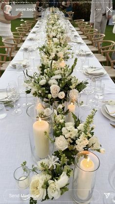 a long table with white flowers and candles on it is set for an outdoor dinner