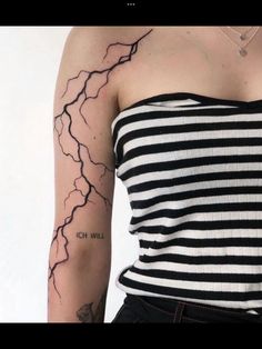 a woman with a black and white stripped shirt has a lightning tattoo on her arm